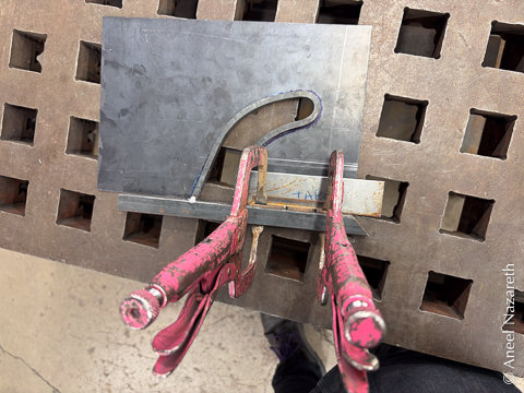 Angle iron is clamped to the bar in preparation for welding. It's spaced from the sheet with a shim labeled TAPE in blue ink
